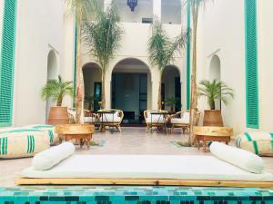 einen Pool mit Tischen, Stühlen und Palmen in einem Gebäude in der Unterkunft Riad Alia in Marrakesch