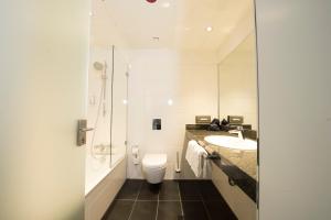 a bathroom with a toilet, sink, and mirror at Carathotel Düsseldorf City in Düsseldorf