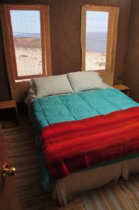 a bed with a colorful blanket in a room with two windows at Hospedaje Boutique Ckamur in Caldera