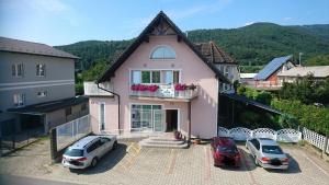 a pink house with two cars parked in a parking lot at Penzion Zeleni Kakadu in Maribor