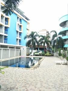 a swimming pool in front of a building with palm trees at Lomsabai Apartments in Bangsaen