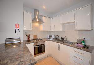 een keuken met witte kasten en granieten aanrechtbladen bij Trinity Mews in Torquay