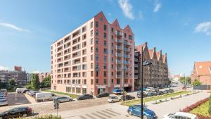 a tall building with cars parked in a parking lot at Dom & House - Apartments Waterlane Island in Gdańsk