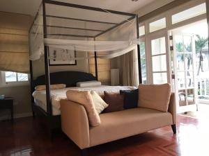 - une chambre avec un lit à baldaquin et un canapé dans l'établissement Baan Dhewaran Beachfront Villa, à Na Jomtien