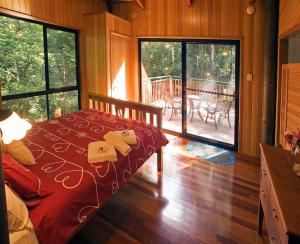 a bedroom with a bed with a red comforter and a deck at Springbrook Lyrebird Retreat in Springbrook
