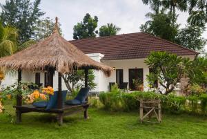 a house with a straw umbrella and chairs in the yard at Blue Marine Resort in Gili Air
