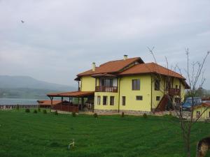 een groot geel huis op een heuvel met een groen veld bij Vila on a Lake Lyastoviche Gnezdo near Troyan in Golyema-Zhelyezna