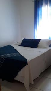 een groot wit bed met blauwe kussens en een raam bij Cantinho Caiçara in Ilhabela