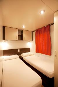 Camping Capalbio في كابالبيو: سريرين في غرفة ذات ستارة حمراء