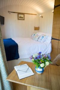 Un dormitorio con una cama y una mesa con un jarrón de flores en GoldenValley Shepherd's Hut en Dorstone