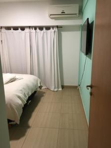 1 dormitorio con 1 cama con cortinas blancas y TV en Deptos Drei Kinder, en Belén de Escobar