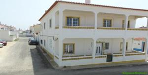 a white building with a car parked in a parking lot at Hostel Nature in Zambujeira do Mar