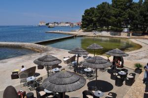 a group of tables and chairs with umbrellas near the water at Hotel Flores in Poreč