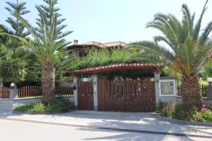 a house with a wooden fence and palm trees at Tosis Apartments in Svoronata