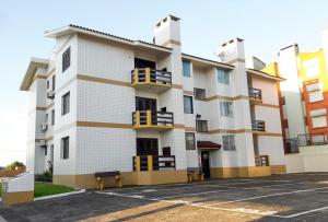 un bâtiment blanc avec des balcons jaunes et un parking dans l'établissement Apartamento Condomínio Mediterranée, à Capão da Canoa