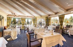 un restaurante con mesas y sillas blancas y ventanas en Bergresort Seefeld en Seefeld in Tirol