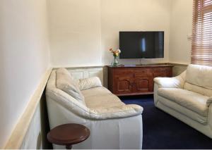 sala de estar con 2 sillas blancas y TV de pantalla plana en Charming Federation style home minutes from CBD en Perth