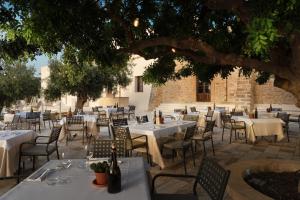 un restaurante con mesas blancas y sillas bajo un árbol en Momentum Wellness Bioresort, en Marinella di Selinunte