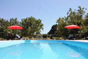 a pool with two red umbrellas and two people sitting at Il Profumo della Natura B&B in Oriolo Romano