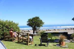 a woman sitting at a table in a yard with the beach at Punakaiki Beach Hostel in Punakaiki