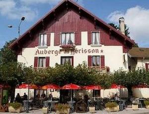 un grand bâtiment rouge et blanc avec des tables et des parasols dans l'établissement Auberge du Hérisson, à La Chaux-du-Dombief