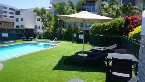 un patio con sillas y una sombrilla junto a la piscina en Pacific Surf Absolute Beachfront Apartments en Gold Coast