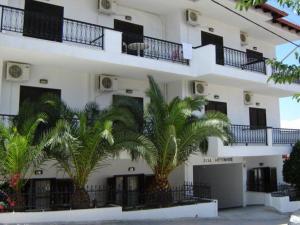 a white building with palm trees in front of it at Elsa Apartments in Pefkochori