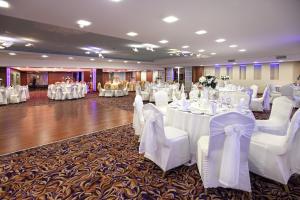 um salão de banquetes com mesas brancas e cadeiras brancas em Surmeli Adana Hotel em Adana