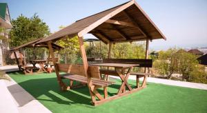 a wooden pavilion with a table and benches on a green lawn at Apartamenty in Veseloe in Adler