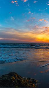 a sunset over the ocean with a rock on the beach at Achtern Diek in Lembruch