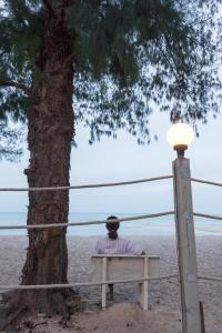 a man sitting on a bench next to a tree at Baan Kratom Tong by the sea in Cha Am