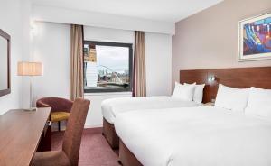 a hotel room with two beds and a desk and a window at Leonardo Hotel Newcastle Quayside in Newcastle upon Tyne
