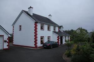 una casa blanca con un coche aparcado delante de ella en Heeneys Lodge B&B, en Donegal