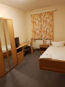 a bedroom with a bed and a desk with a television at Hotel Merkur Garni in Sarstedt