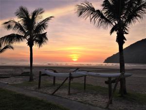 a beach with two palm trees and a bench with a surfboard at Bertioga Beach Hostel in Bertioga