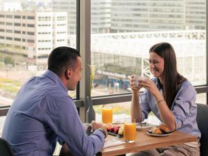 Een man en een vrouw aan een tafel die sinaasappelsap drinken. bij Mercure Amsterdam Sloterdijk Station in Amsterdam