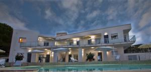 a large white building with a balcony and a swimming pool at Cala Del Faro Beach Villas in Cittadella del Capo