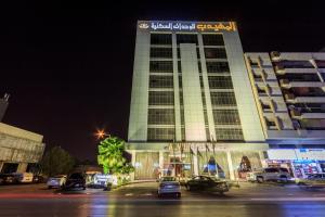 Al Muhaidb Al Olaya Suites في الرياض: مبنى فيه سيارات تقف امامه ليلا