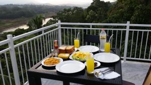 a table with plates of food and drinks on a balcony at Mahaweli View Inn Kandy in Kandy