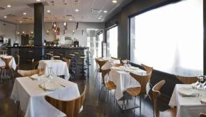 un restaurante con mesas y sillas blancas y un bar en Hotel Valcarce León, en Onzonilla