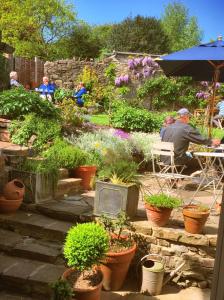 Bridge House في Bampton: رجل يجلس على طاولة في حديقة بها نباتات