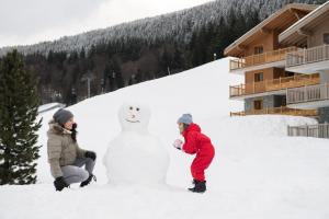 two people making a snow man in the snow at CGH Résidences & Spas Les Chalets de Jouvence in Les Carroz d'Araches