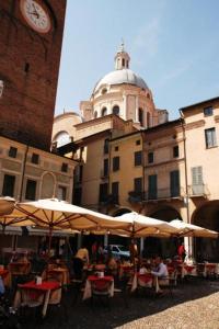 una cafetería al aire libre con mesas y sombrillas y una torre del reloj en Casa Margherita en Mantua