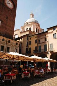ein Café im Freien mit Tischen und Sonnenschirmen und einem Uhrturm in der Unterkunft Casa Margherita in Mantua