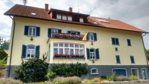 une maison jaune avec volets bleus et fleurs rouges dans l'établissement Ferienwohnung Mülhaupt, à Ühlingen-Birkendorf