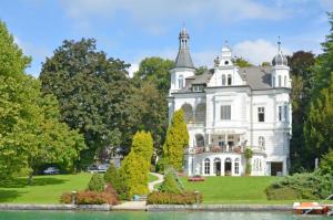 una gran casa blanca en un césped junto a un lago en Dermuth Hotels – Parkvilla Wörth, en Pörtschach am Wörthersee