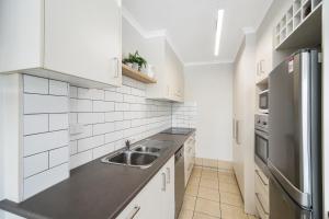 a white kitchen with a sink and a refrigerator at Renovated Moololaba Unit 100m To Beach in Mooloolaba