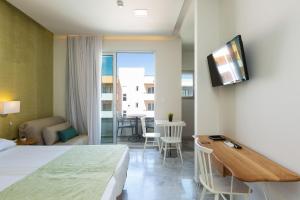 レティムノ・タウンにあるMeltemi Coast Suitesのベッド、テーブル、テレビが備わるホテルルームです。