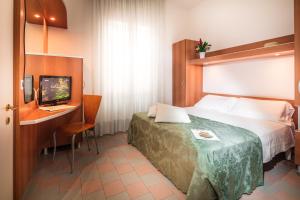 Habitación de hotel con cama, escritorio y TV. en Park Hotel en Lignano Sabbiadoro
