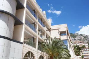 a white building with a palm tree in front of it at Appart'hôtel Odalys City - Monaco Les Hauts de la Principauté in Beausoleil